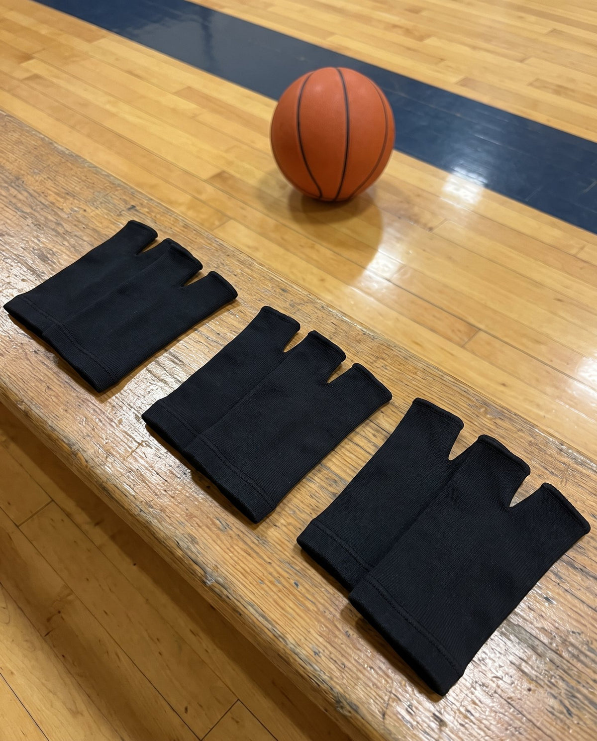 Six Olyra Blister Sleeves, three pairs, laid out on a gym bench next to a basketball