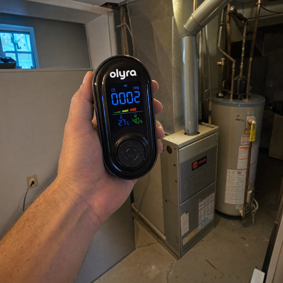 A hand holding the TrueDetect detector showing 2 PPM beside a basement furnace and water heater.