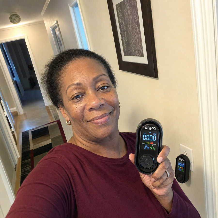 A woman holding the TrueDetect detector in a hallway, with a second detector plugged into the wall behind her.